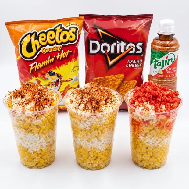 Three cups of Mexican corn with Cheetos, Doritos and Tajín behind them