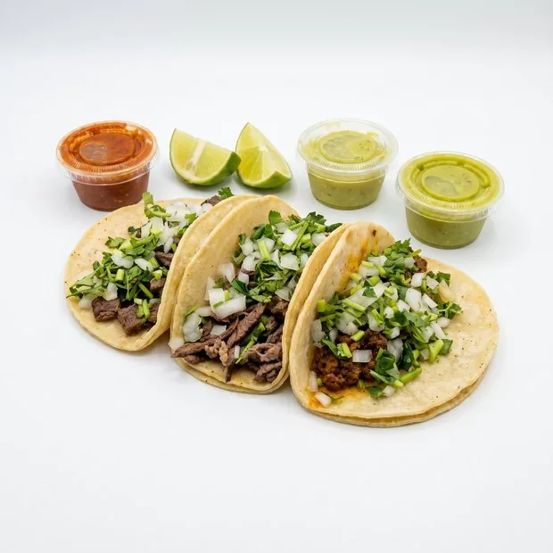 Three street tacos with onion and cilantro, red and green salsa, lime